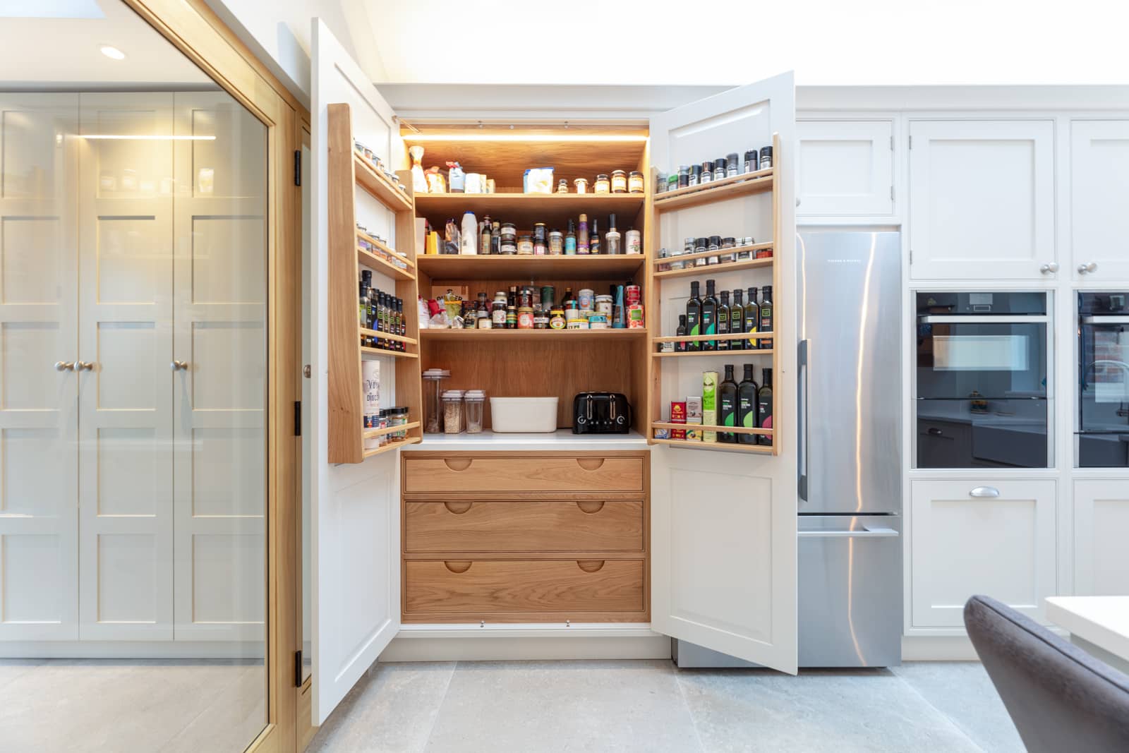 A kitchen with an open pantry and a refrigerator.