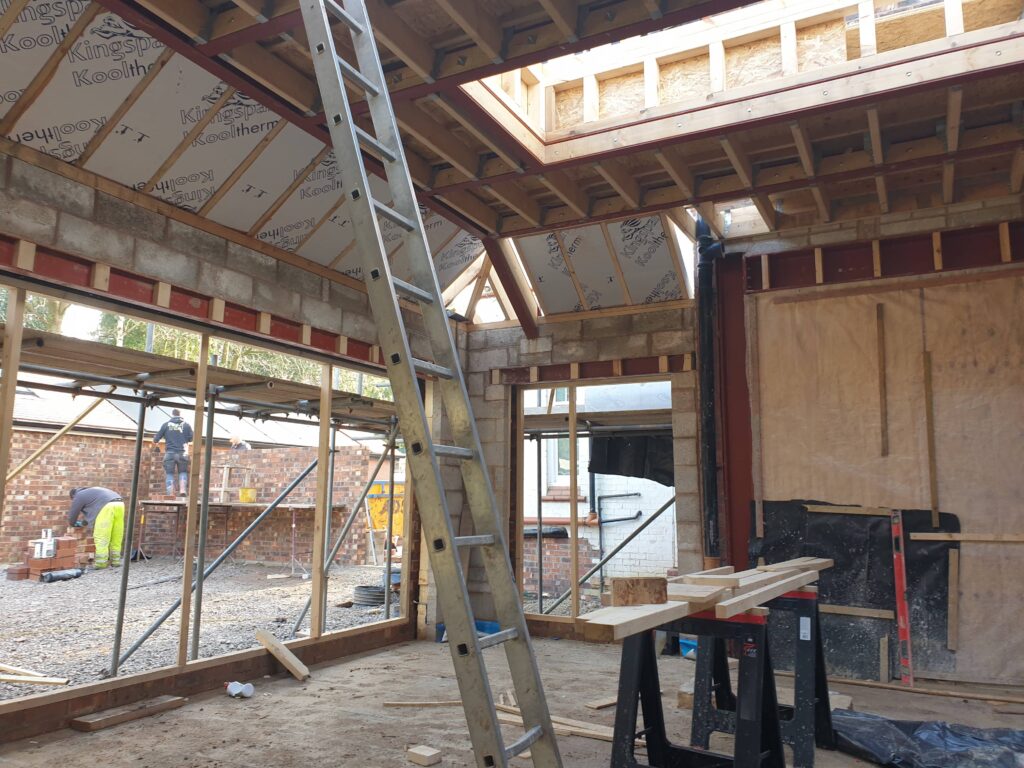 Construction site with workers, scaffolding, exposed roof framework, and a scenic view.