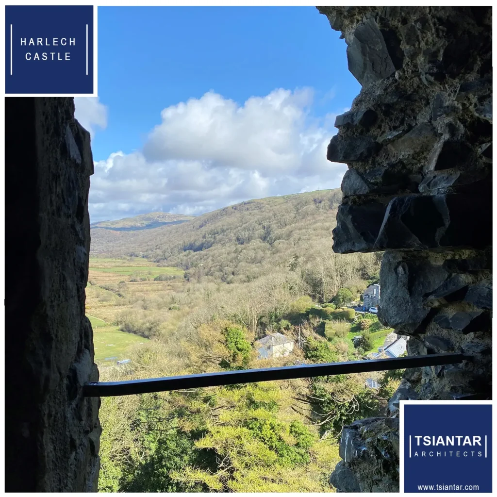 View through an ancient stone window at Harlech Castle in North Wales, overlooking lush green fields and distant mountains under a partly cloudy sky.