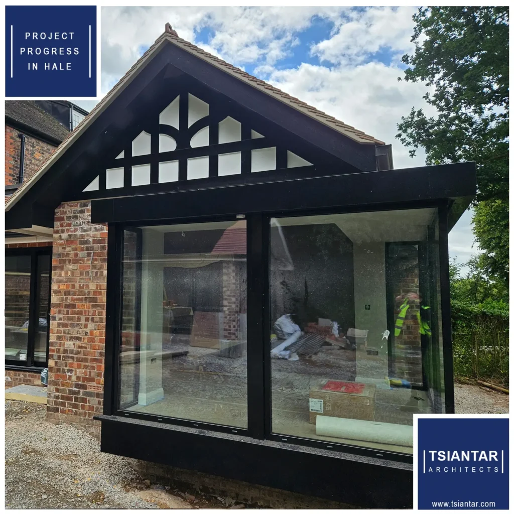 Exterior view of a modern house extension under construction in Hale, featuring large glass windows and a brick facade with a projected triangular roof. Builders are visible through the windows, highlighting the project's progress.