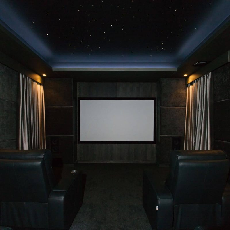 A home theater with black leather chairs and a projector screen.